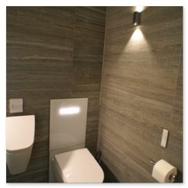 Der Raum zeigt eine stilvolle Toilette und ein Waschbecken, umgeben von schlichten, grauen Wänden und sanfter Beleuchtung.