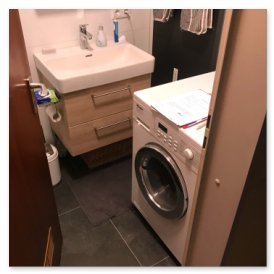 In einem kleinen Badezimmer sind ein Waschbecken mit Schubladen und eine Waschmaschine sichtbar, die ordentlich angeordnet sind.