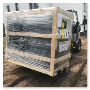 Ein mit Folie umwickelter Holzrahmen, der auf einem Baustellenboden steht, während ein Gabelstapler in der Nähe ist.