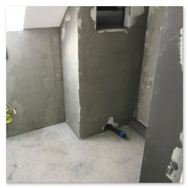 Der Raum zeigt eine glatte, graue Wand mit einem kleinen Fenster und einem Rohr, das auf bevorstehende Installationen hindeutet.