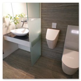 Das Badezimmer zeigt ein minimalistisches Design mit einem schwebenden Waschbecken und einer separaten Toilette, umgeben von grauen Fliesen.
