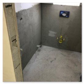 Der Raum zeigt eine glatte, graue Wand mit einem sichtbaren Wasseranschluss und einem Abfluss, bereit für die Installation.