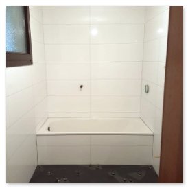 Die Badewanne steht in einem modernen, gefliesten Raum mit einem Fenster, das Tageslicht hereinlässt und eine ruhige Atmosphäre schafft.