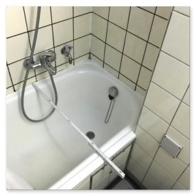 In einer kleinen Badezimmer-Ecke steht eine Badewanne, die mit einer Duschstange und einem Wasserhahn ausgestattet ist.