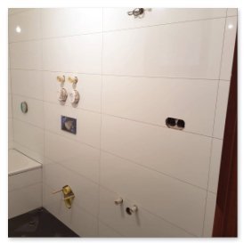 Die Wand zeigt mehrere ungenutzte Wasseranschlüsse und Halterungen, die auf Renovierungsarbeiten im Badezimmer hindeuten.