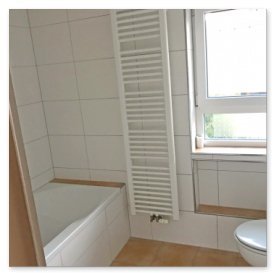 Das Badezimmer zeigt eine moderne Badewanne, einen weißen Heizkörper und einen Blick nach draußen durch ein großes Fenster.