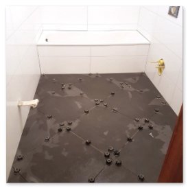 In einem Badezimmer sind die Fliesen auf dem Boden unregelmäßig angeordnet, umgeben von Abstandshaltern und einer Badewanne im Hintergrund.