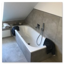 Die Badewanne ist mit einem Duschkopf ausgestattet und von einem hellen, minimalistischen Raum umgeben.