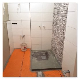 Ein Badezimmer mit einem unvollendeten Duschbereich, der mit grauen Fliesen und einem strukturierten Wanddesign ausgestattet ist.