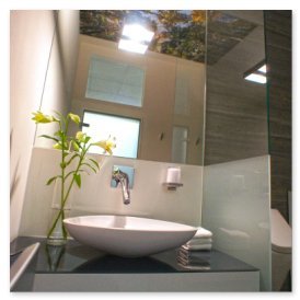 Das Waschbecken in einem hellen Badezimmer spiegelt die natürliche Beleuchtung und eine grüne Pflanze wider.