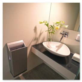 Der Raum zeigt ein minimalistisches Design mit einem runden Waschbecken, einem Handtuch und einem Abfalleimer aus Metall.