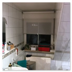 Ein Badezimmer mit weißen Fliesen, einem Fenster mit Jalousien und einem Waschbecken, das mit Pflegeprodukten dekoriert ist.