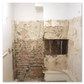 Eine verfallene Wand mit abblätternder Farbe und freiliegenden Ziegeln, die den Zustand des Raumes verdeutlicht.