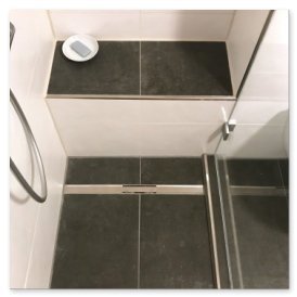 Ein Blick auf eine stilvolle Dusche mit dunklen Fliesen, einem Duschkopf und einer Seife auf einer schlichten Ablage.