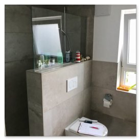 Die Dusche ist durch eine Glaswand abgetrennt, während auf dem Waschbecken verschiedene Pflegeprodukte stehen.